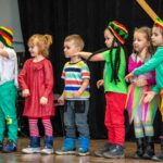 Sześcioro kolorowo ubranych dzieci stoi w rzedzie na scenie